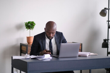 Fototapeta na wymiar Young African executive reading documents and working on a laptop while sitting at his desk in an office. soft focus