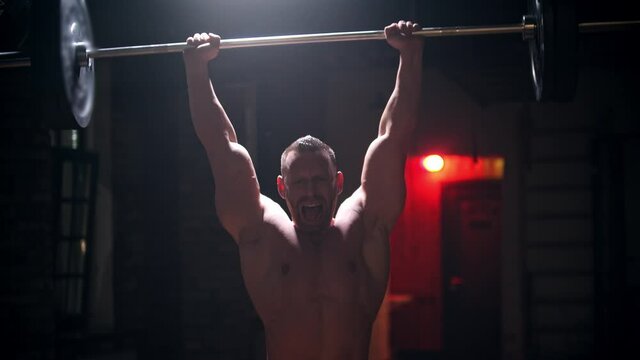 Tough man in the gym doing exercises - pulling up a heavy bar with an effort