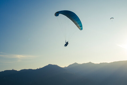 Adventurer flying  in the skyes of Nepal, Asia. Silhouette of a chain of mountains in the background and sun shinning from behind the hills. Extreme sports post pandemic adventure concept.