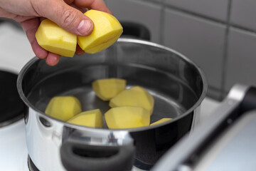 Potatoes are boiled in a saucepan. A man puts potatoes in a pot. Process. Close-up.