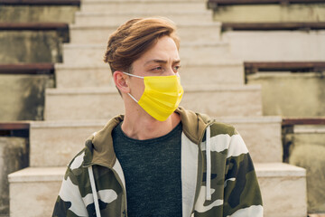 Fototapeta na wymiar Athletic young and handsome man in sportswear wearing a yellow mask. Attractive male model wearing a yellow medical mask due to Covid-19 measures. Caucasian man wearing a mask to protect himself 
