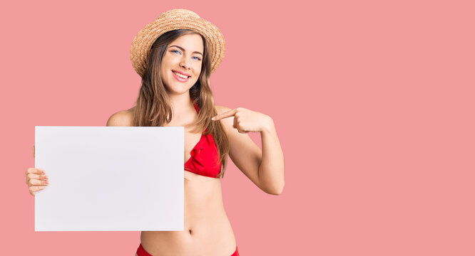 Beautiful caucasian young woman wearing bikini holding blank empty banner pointing finger to one self smiling happy and proud