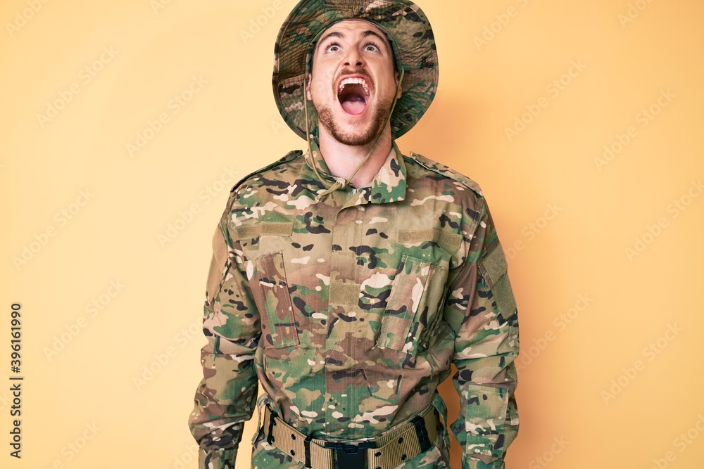 Wall mural Young caucasian man wearing camouflage army uniform angry and mad screaming frustrated and furious, shouting with anger. rage and aggressive concept.