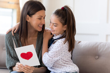 Small caring Caucasian girl child greeting young mother with birthday anniversary present handmade...