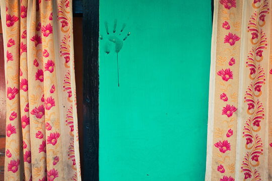 Peculiar hand print stamp on a teal green wall and colorful curtains on the sides. Inside architecture from Pokhara, Nepal.