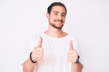 Young handsome man wearing casual white tshirt success sign doing positive gesture with hand, thumbs up smiling and happy. cheerful expression and winner gesture.