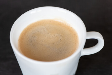 Black aroma coffee in the white cup on black background. Close up view