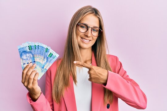 Young blonde woman wearing business style holding south african rands banknotes smiling happy pointing with hand and finger