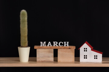 Wooden calendar of March, cactus and house model on black background. Copy space