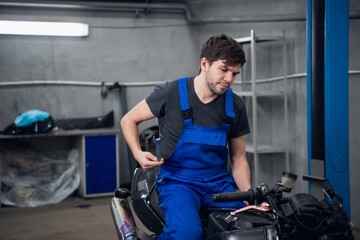 Repairer sitting on a motorcycle with a tool in his hand