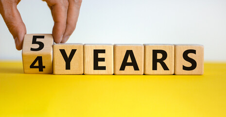 5th anniversary. Male hand turns cubes and changes the expression '4 years' to '5 years'. Beautiful yellow table, white background. Business and 5th anniversary concept, copy space.