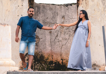 Naklejka na ściany i meble Two beautiful models, a young married couple, mother to be pregnant lady, holding hands, and looking at her husband standing portrait in front of ruins of Galle Dutch fort.