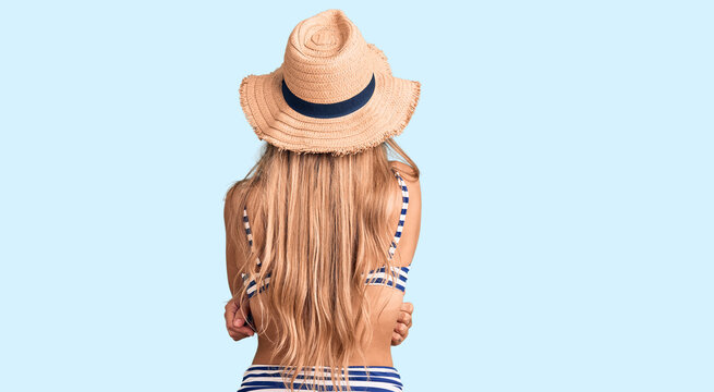 Young beautiful blonde woman wearing bikini and hat standing backwards looking away with crossed arms