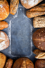A variety of breads surrounded by a silhouette wooden cutting board on a gray surface, top view, copy space. Food bakery shop concept background.