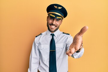 Handsome hispanic man wearing airplane pilot uniform smiling friendly offering handshake as greeting and welcoming. successful business.