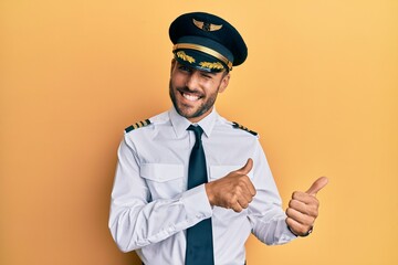 Handsome hispanic man wearing airplane pilot uniform pointing to the back behind with hand and...