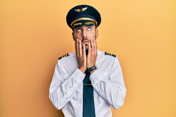 Handsome hispanic man wearing airplane pilot uniform tired hands covering face, depression and sadness, upset and irritated for problem