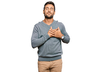 Handsome hispanic man wearing casual clothes smiling with hands on chest with closed eyes and grateful gesture on face. health concept.