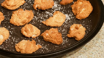 Soft golden coconut cookies shaped like clouds on a black plate sprinkled with coconut