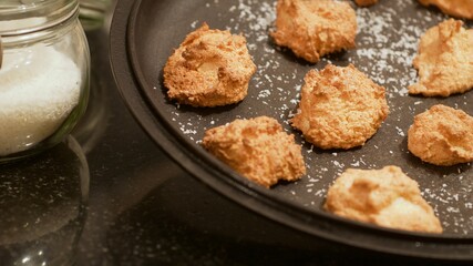 Soft golden coconut cookies shaped like clouds on a black plate sprinkled with coconut