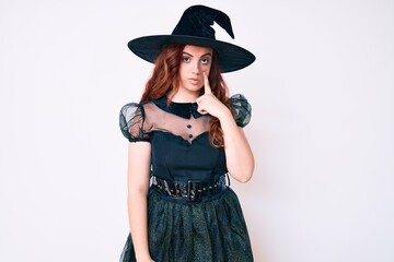 Young beautiful woman wearing witch halloween costume pointing to the eye watching you gesture, suspicious expression