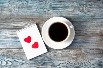 White coffee mug and two red hearts on a Notepad on a wooden background. The view from the top. The Concept Of Valentine's Day.