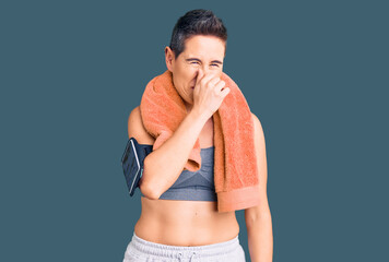 Young woman with short hair wearing sportswear and towel using smartphone smelling something stinky...
