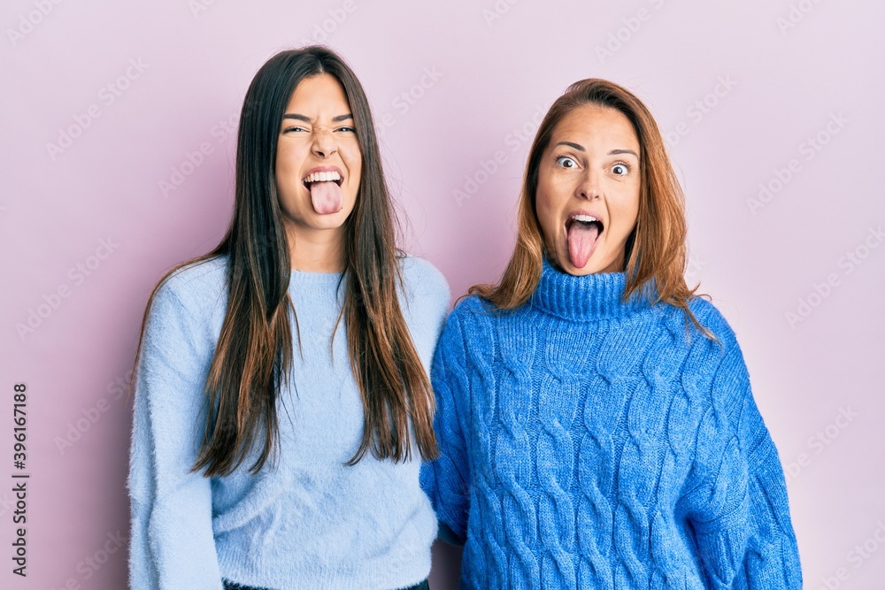 Wall mural Hispanic family of mother and daughter wearing wool winter sweater sticking tongue out happy with funny expression. emotion concept.