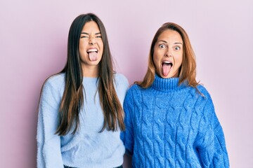 Hispanic family of mother and daughter wearing wool winter sweater sticking tongue out happy with funny expression. emotion concept. © Krakenimages.com