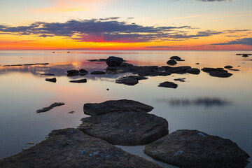 Beautiful colorfull sunset over the sea shore with rocks under shallow water