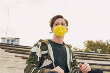 Athletic young and handsome man in sportswear wearing a yellow mask. Attractive male model wearing a yellow medical mask due to Covid-19 measures. Caucasian man wearing a mask to protect himself 