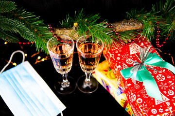 Christmas background with fir branches, two champagne glasses, gift, medical mask, concept of New Year's decor.