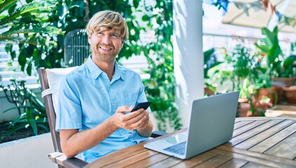 Middle age handsome man working at home using computer laptop and smartphone