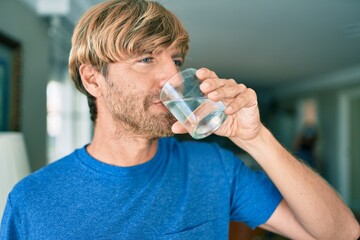 Fototapeta na wymiar Young irish man drinking glass of water standing at home