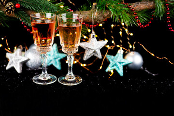 New Year and Christmas decor. Glasses for champagne, toys for the Christmas tree stand on the table in front in the dark, beautiful bokeh on the background. Close-up.