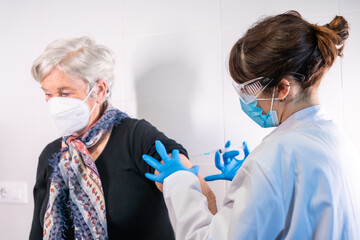 An elderly woman receiving the injection of the coronavirus vaccine by a doctor to receive the...