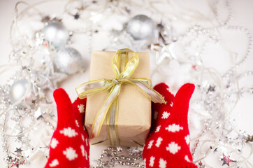 Female hands hold a Christmas gift with a gold ribbon in red mittens, new year mood, preparation for the celebration. Top view, close-up.