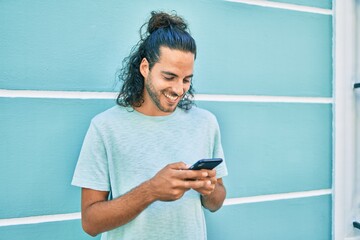 Young hispanic man smiling happy using smartphone leaning on the wall