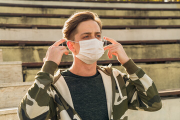 Young handsome man wearing a white medical mask poses while straightening his mask. Images of the man wearing a mask due to the pandemic from various angles.