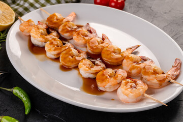 grilled tiger shrimp skewer. The seafood on the skewers in the pan Asian sauce on a white plate. For the restaurant menu