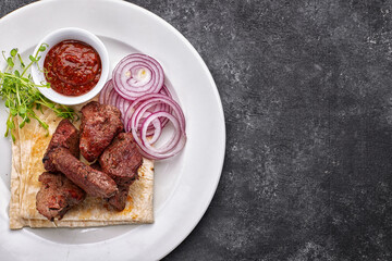shashlik, with sauce, onions, and lavash, on a white plate, on a dark background