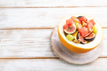 Vegetarian fruit salad of watermelon, grapes, figs, pear, orange, cashew on white wooden background. Side view, copy space.