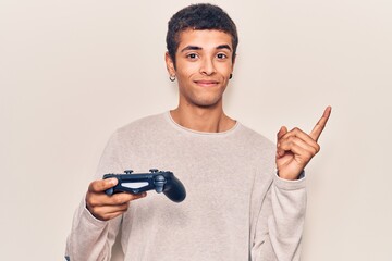 Young african amercian man playing video game holding controller smiling happy pointing with hand...