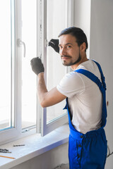 Male repairer in overalls installs a window and poses at the camera