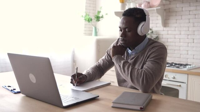 Serious african black business man, male student wears headphones talking, conference video calling, social distance learning remote class or course, working distantly using laptop at home office.