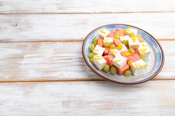 Obraz na płótnie Canvas Vegetarian salad with watermelon, feta cheese, and grapes on blue ceramic plate on white wooden background. Side view, copy space.