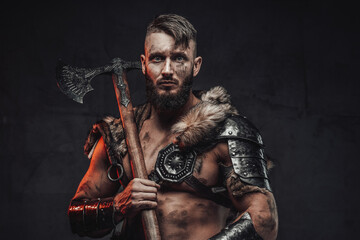 Fototapeta premium Armed with huge two handed axe nordic barbarian in light armour in dark background.