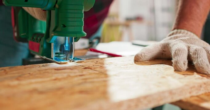Young carpenter cuts an osb board with a jigsaw. Craftsman's hands in cloth protective gloves. The jigsaw blade cuts precisely.