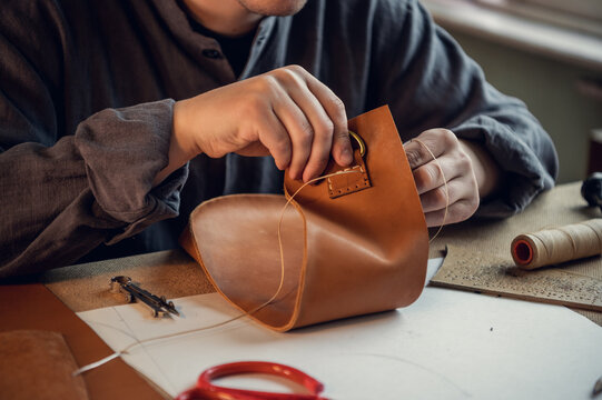 An experienced tanner sews a clasp for a leather product with stitches.