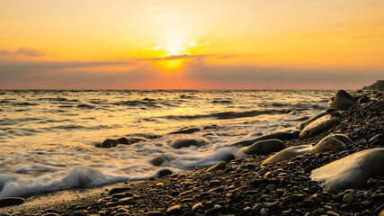 Obraz premium Sunset at the sea. Pebble beach and surf at sunset. Long exposure shooting. Focusing on water's edge and pebbles.